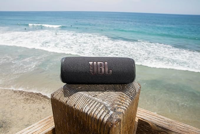 JBL portable Bluetooth speaker on wooden post by the beach — waterproof, travel-ready speaker with powerful sound, one of the best portable speakers on Amazon 2025